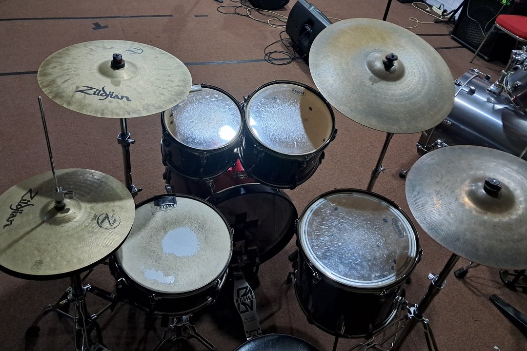 A full-size five-piece acoustic drum kit seen from the drummer's throne, with a snare, two rack toms, a floor tom, hi-hats and two crash cymbals