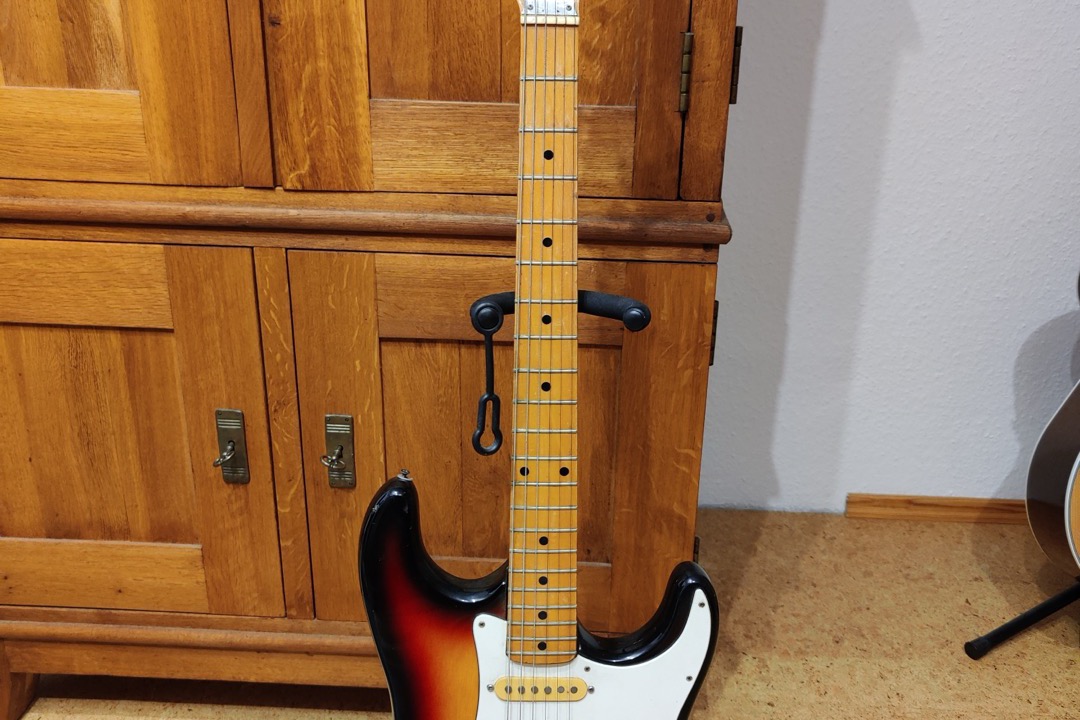 Beginner electric guitar with a sunburst Stratocaster body resting against a practice amp