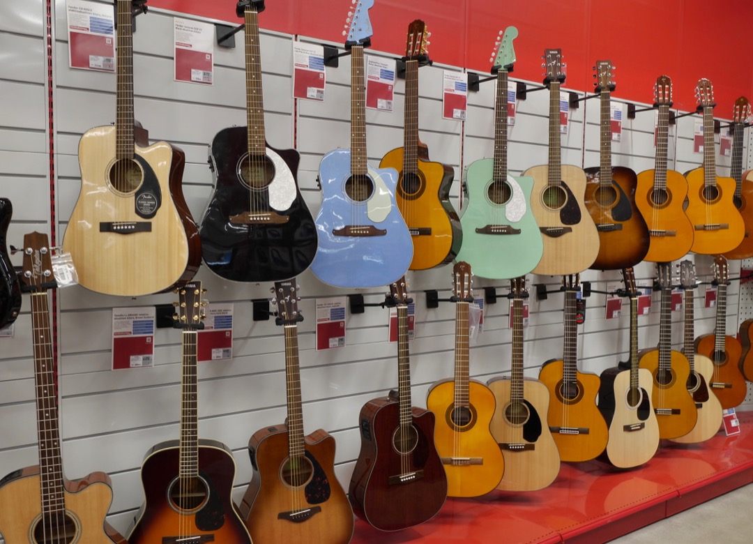 A wall of affordable acoustic guitars on display with price tags in a music store