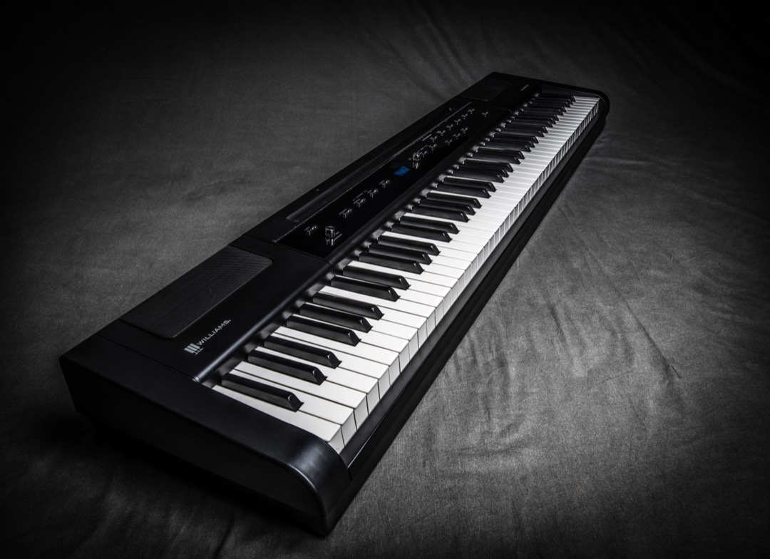 An 88-key hammer-action digital piano photographed at an angle on a dark backdrop, showing the full keybed and the control panel above it