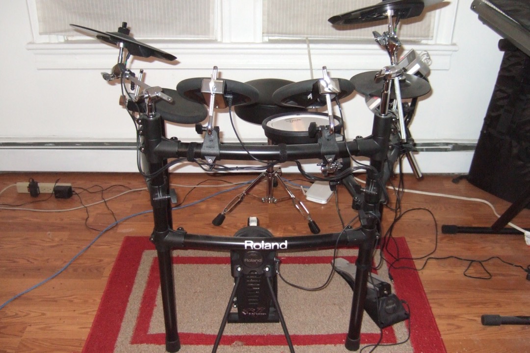 A Roland V-Drums electronic drum kit set up on a rug in a home practice room, showing the rack, mesh pads and cymbal arms of a typical apartment-friendly kit