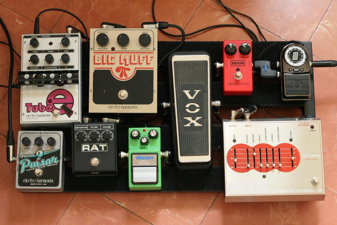 A guitar pedalboard loaded with classic effects pedals — overdrive, fuzz, wah, compressor, delay and tuner — the range of stompboxes a guitarist chooses between