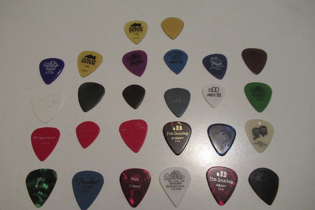 An assortment of guitar picks in different colors, materials, and thicknesses laid out on a flat surface
