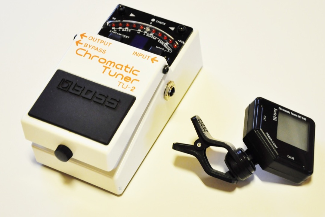 Clip-on chromatic tuner attached to an acoustic guitar headstock showing the tuned note
