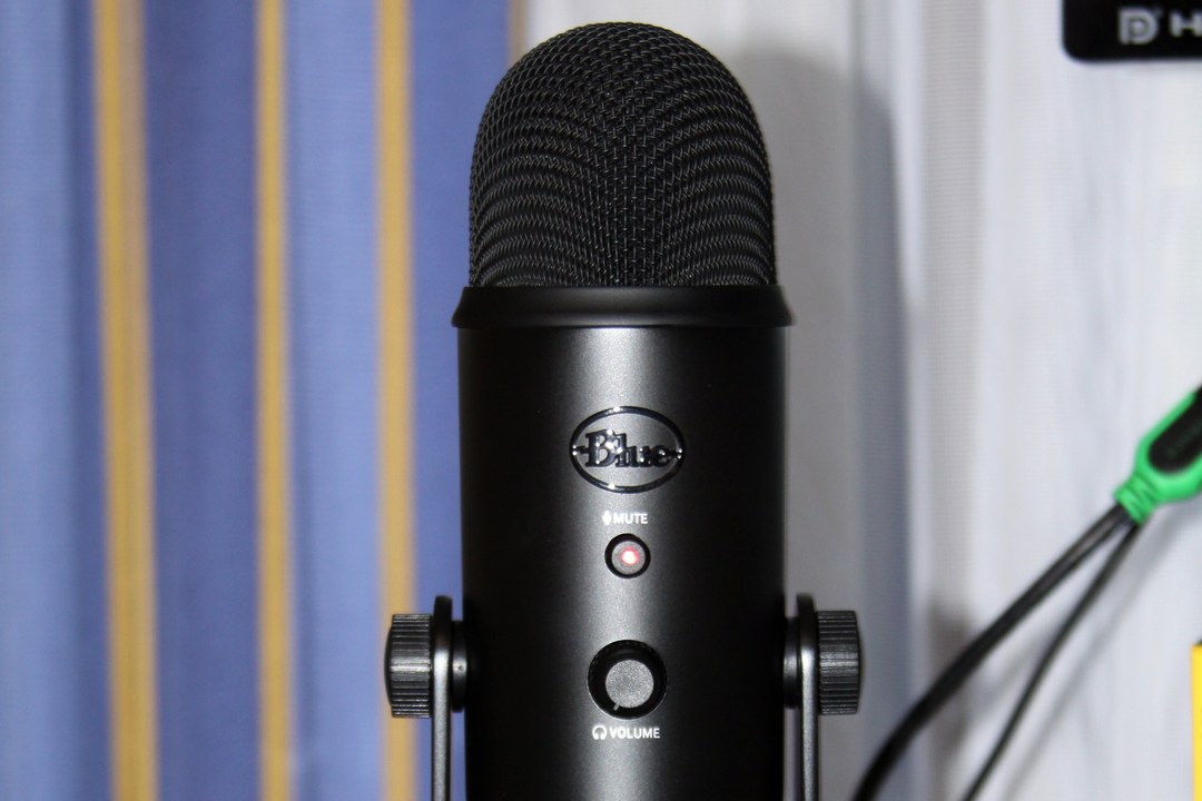 A Blue Yeti Blackout USB condenser microphone on its desktop stand, showing the mute indicator and headphone volume controls