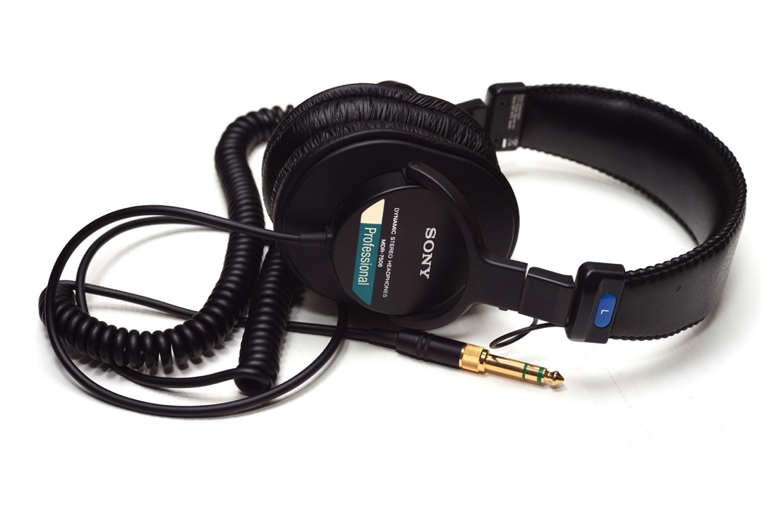 Sony MDR-7506 closed-back studio headphones on a white background, with the coiled cable and gold 1/4-inch adapter in the foreground