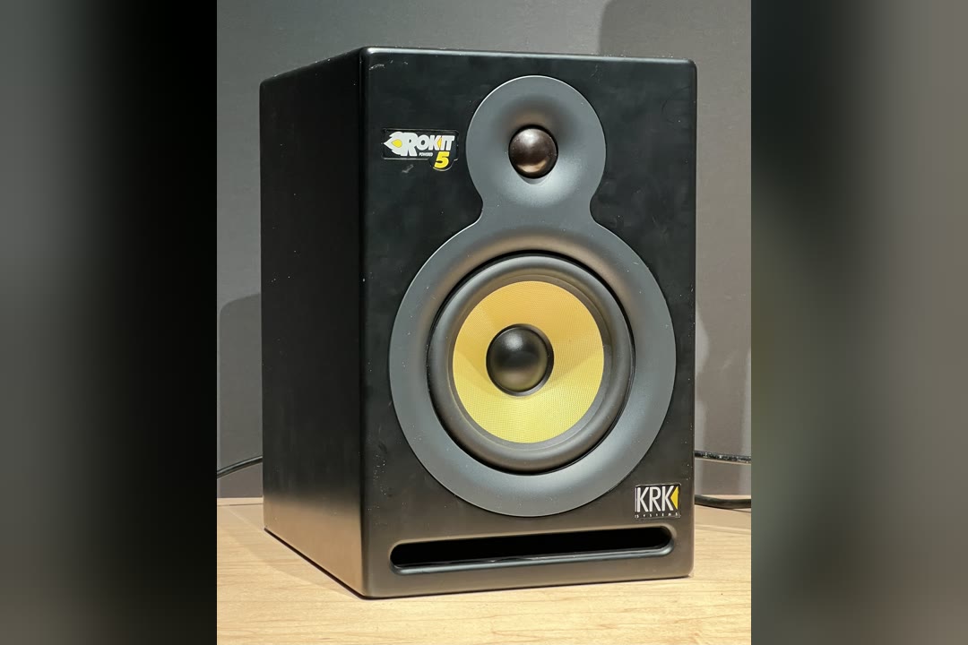 KRK Rokit 5 powered studio monitor with its yellow woven woofer, sitting on a wooden desk