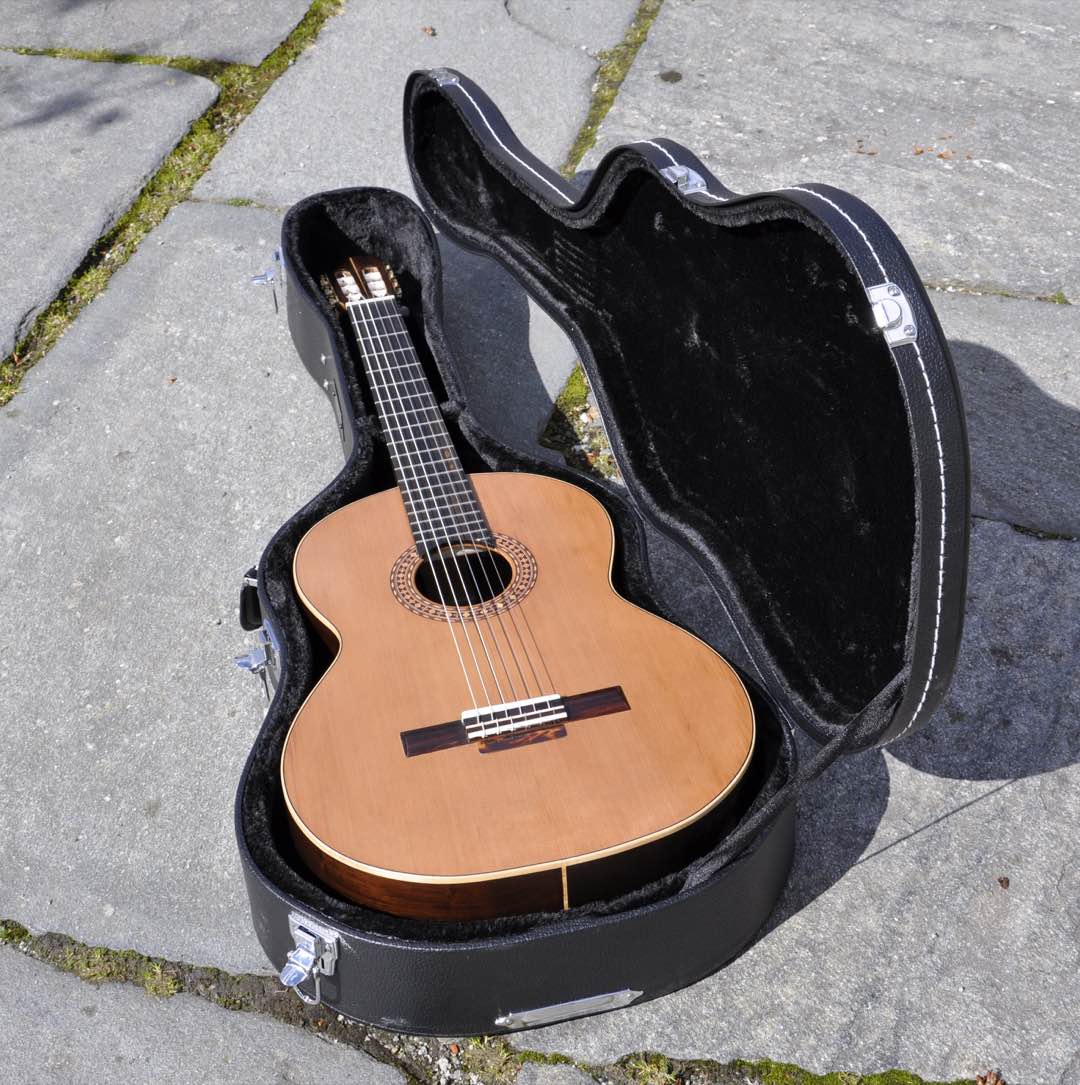 A nylon-string classical guitar with a cedar top resting in an open hard case