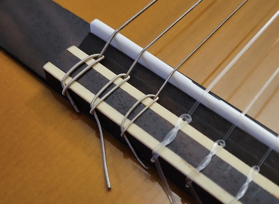 Close-up of a classical guitar tie block showing clear nylon treble strings and silver-plated copper wound basses knotted at the bridge