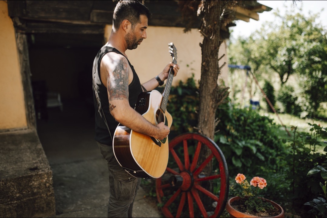 A musician playing an acoustic guitar outdoors, strumming an open-chord song