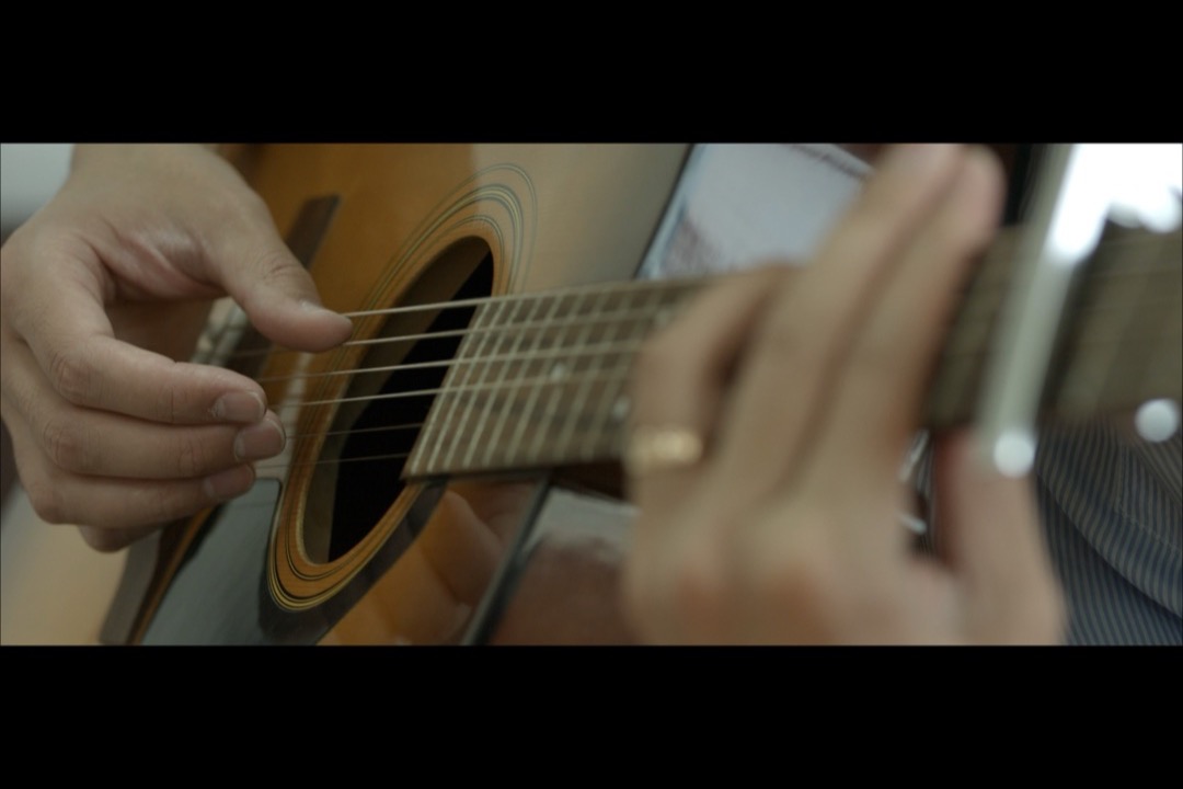 Close-up of a beginner's left hand fretting an open chord on an acoustic guitar neck