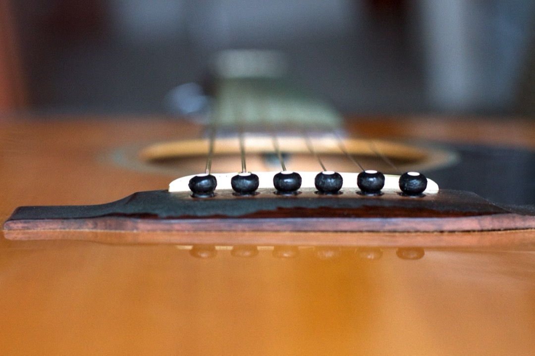 Close-up of an acoustic guitar bridge with six black bridge pins holding the strings in place