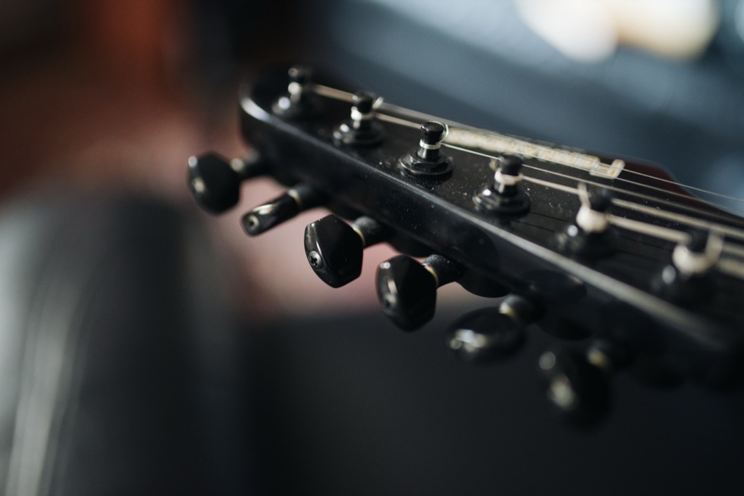 Close-up of a hand turning a tuning peg on an acoustic guitar headstock