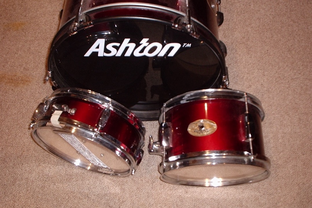 A small three-piece junior drum set with a 16-inch bass drum, a 10-inch snare and a 10-inch tom, the kind of kit sized for a young child