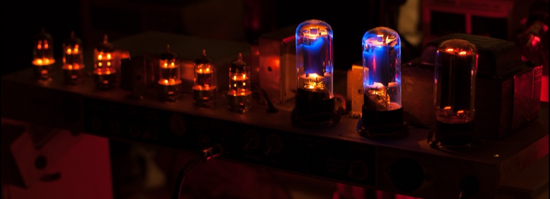 The glowing vacuum tubes on the chassis of a Fender Bandmaster Reverb tube guitar amplifier, viewed from above